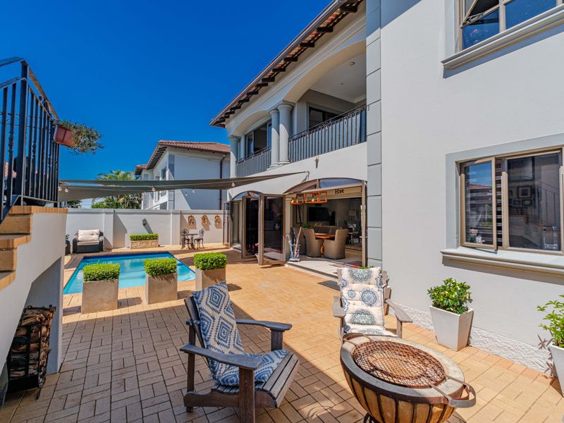 A well-maintained rear exterior featuring a paved patio, swimming pool, and a covered balcony with metal railings and folding glass doors.