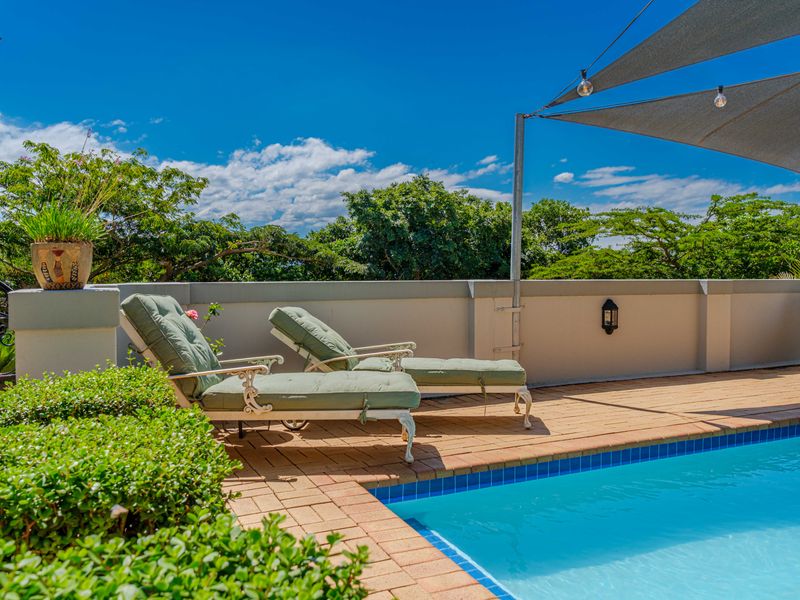 Outdoor pool area featuring a paved deck, masonry boundary wall, and a shade sail, providing a pleasant space for relaxation and recreation.
