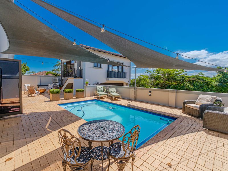 A well-maintained outdoor pool area featuring a paved deck, a large shade sail, and perimeter walling, perfect for outdoor relaxation and entertainment.