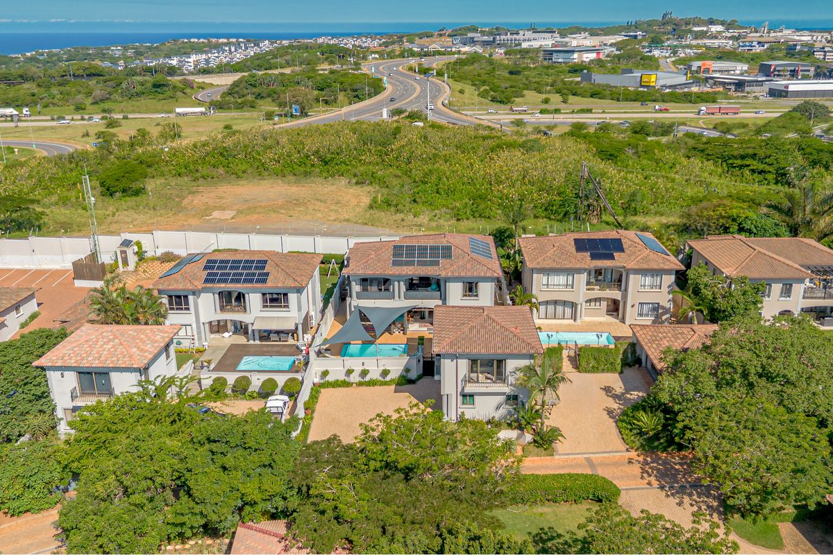 Aerial view of a residential complex featuring multiple homes with tiled roofs, solar panels, private swimming pools, and paved driveways in a suburban setting.