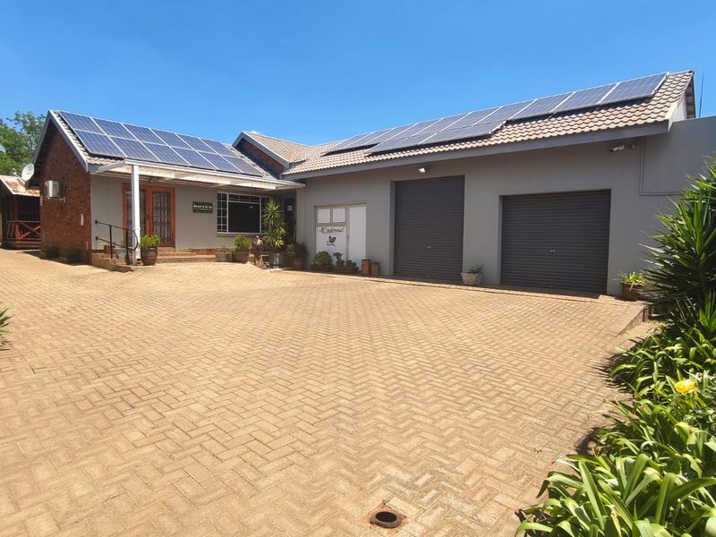 Front exterior view of the property featuring a large paved driveway, double garage with roller shutter doors, and extensive roof-mounted solar panels.