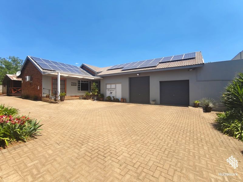 Front elevation of a well-maintained house featuring a paved driveway, double garage with roller doors, and extensive roof-mounted solar panels.