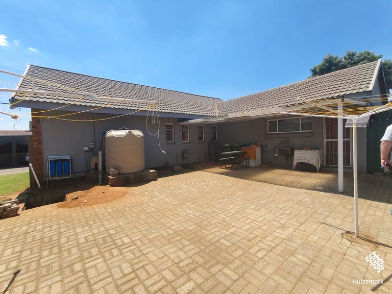 Rear exterior view featuring a paved patio area, water storage tank, filtration system, and an external sink against the house wall.