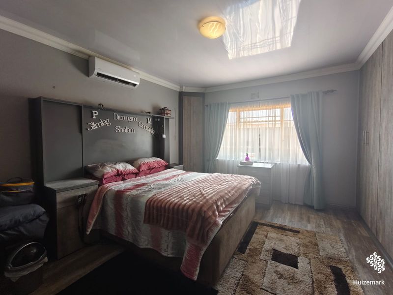 A bedroom featuring built-in cupboards, a custom headboard, laminate flooring, and an air conditioning unit.