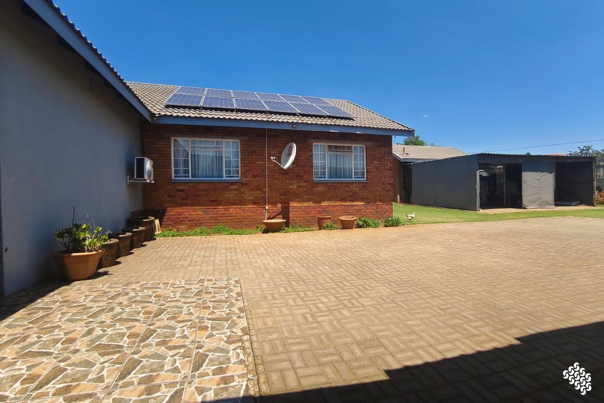 Rear exterior view featuring a brick facade, solar panel installation, paved driveway, and a covered carport area.