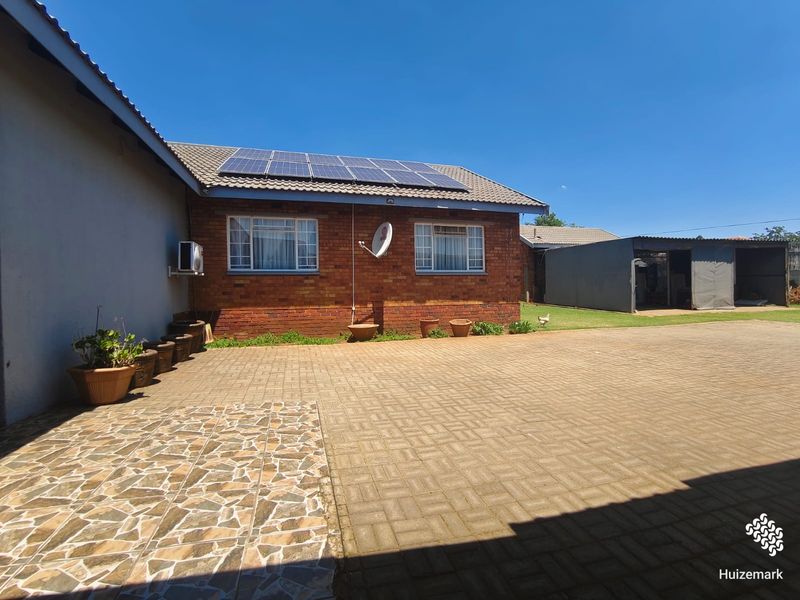 Rear exterior view featuring a brick facade, solar panel installation, paved driveway, and a covered carport area.