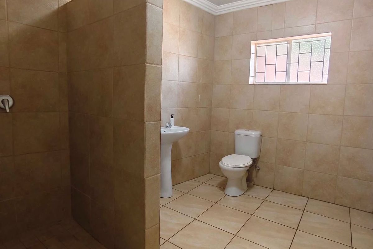 A spacious, tiled bathroom featuring a walk-in shower, pedestal washbasin, and toilet, finished with neutral ceramic tiling and a functional layout.