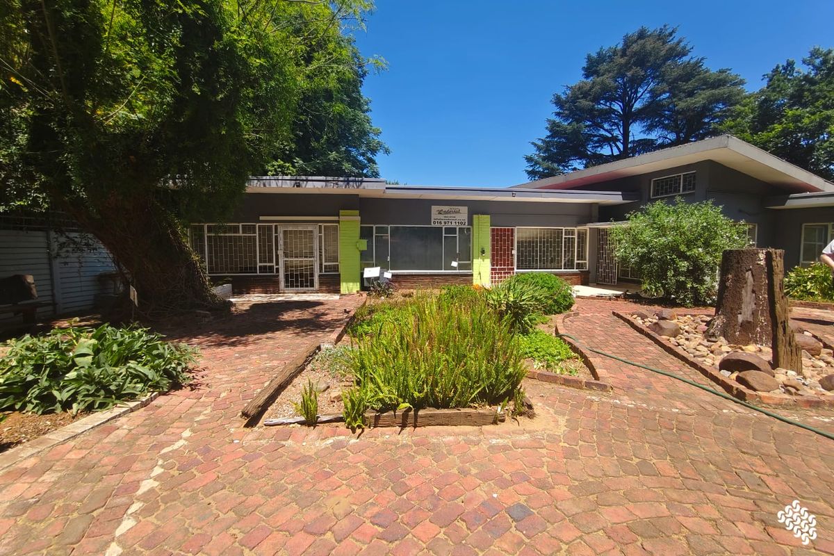 A rear exterior view of the property featuring a brick-paved courtyard, established garden beds, and secure window and door treatments.