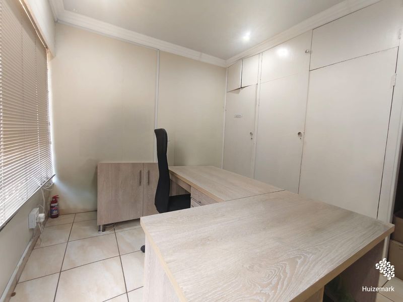 A functional home office featuring tiled flooring, built-in storage cupboards, and venetian blinds, providing a practical workspace.