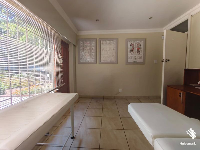 A functional office or treatment room featuring tiled flooring, recessed lighting, and large windows with venetian blinds, suitable for professional or clinical use.