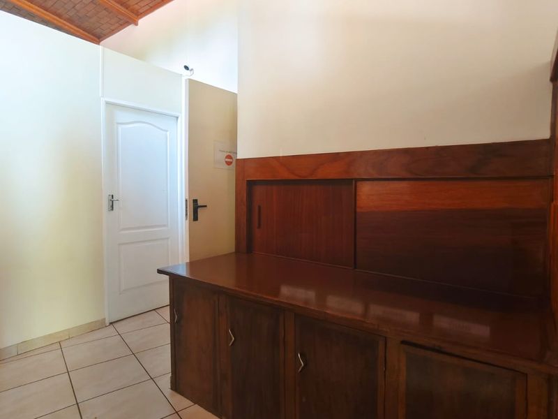 A hallway featuring tiled flooring, built-in wooden cabinetry, and an exposed timber ceiling, providing a functional transition space within the home.