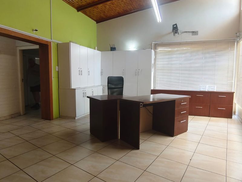 Spacious home office featuring tiled flooring, extensive built-in cabinetry, and a distinctive exposed timber ceiling with natural light.