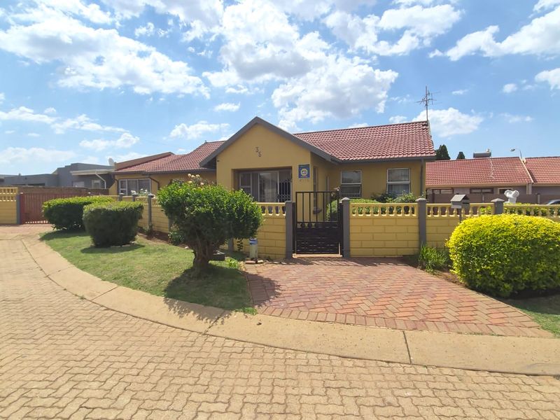 Front elevation of a single-story house featuring a tiled roof, brick-paved driveway, and a secure gated entrance with established garden landscaping.
