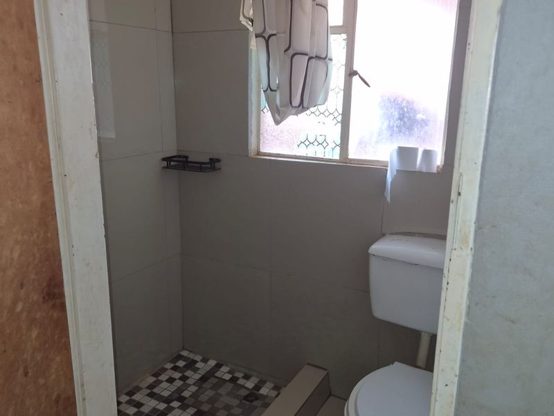 A compact bathroom featuring a shower area with tiled flooring, a standard toilet, and neutral wall tiling.