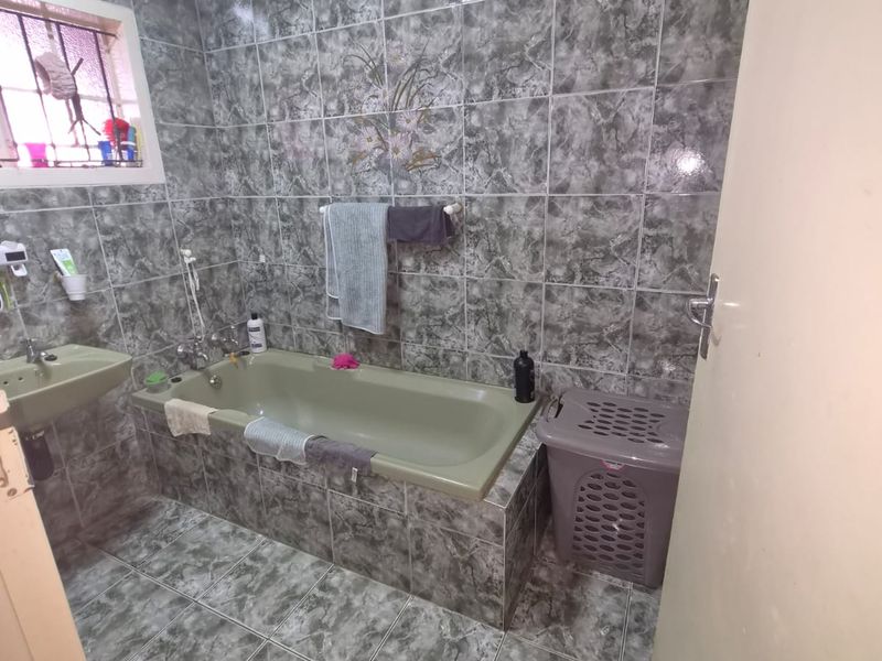A functional bathroom featuring full-height marble-effect wall tiling, a built-in bathtub, and a wall-mounted basin.