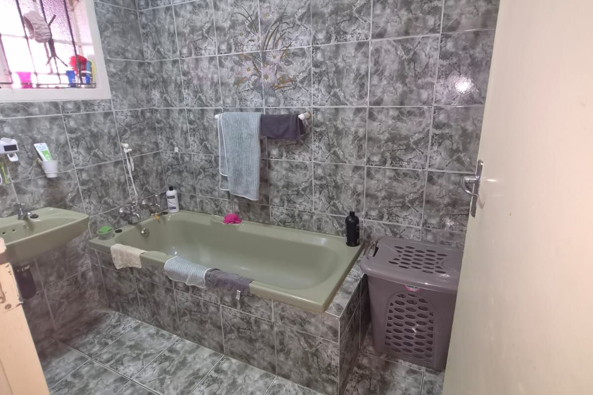 A functional bathroom featuring full-height marble-effect wall tiling, a built-in bathtub, and a wall-mounted basin.