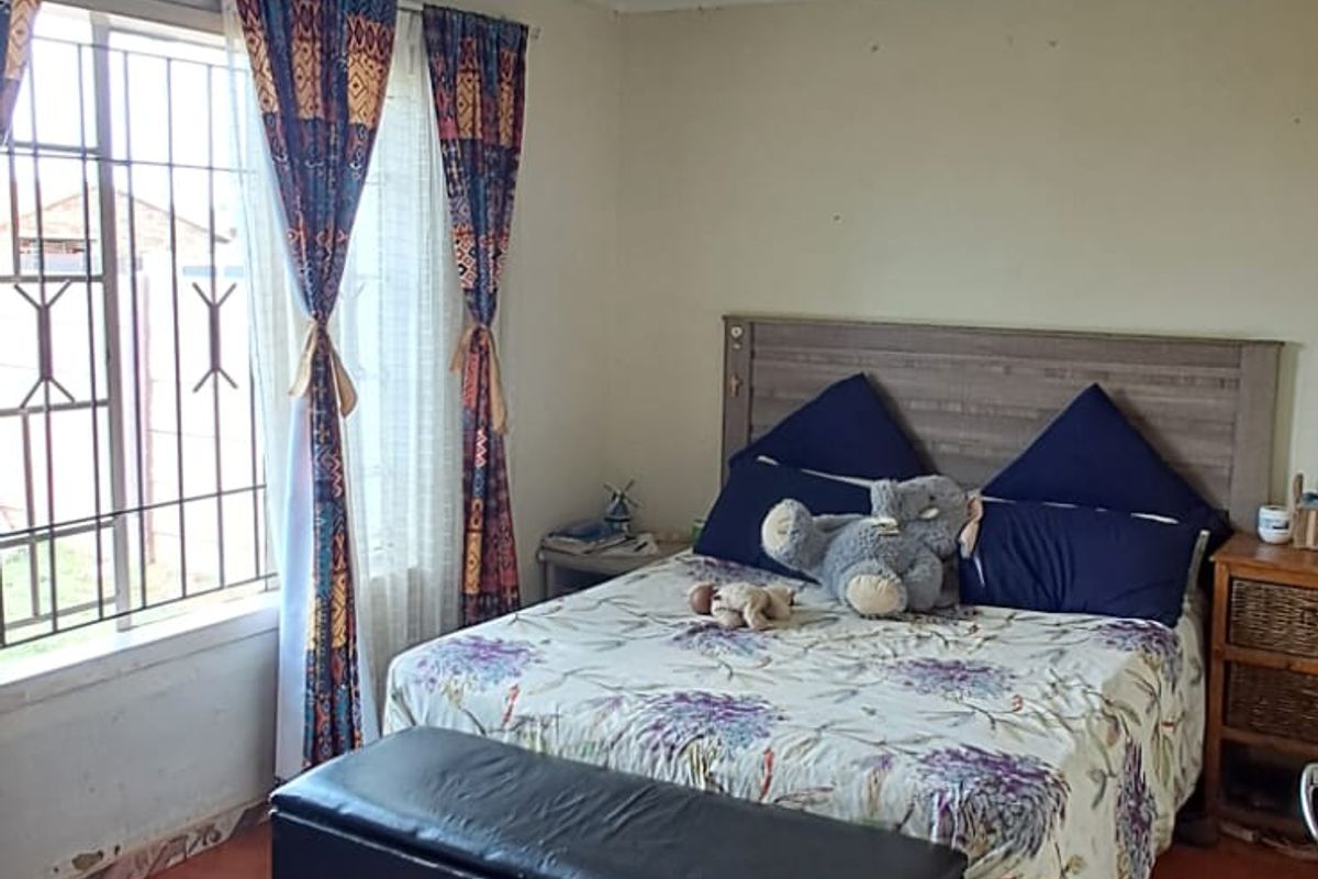 A bedroom featuring tiled flooring, security bars on the window, and a ceiling light fixture. The room shows signs of wear on the walls.