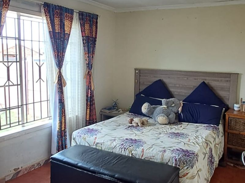 A bedroom featuring tiled flooring, security bars on the window, and a ceiling light fixture. The room shows signs of wear on the walls.