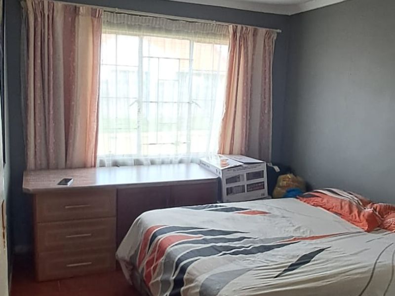 A bedroom featuring tiled flooring and a window with security bars. The room requires cosmetic updates to improve its overall condition.