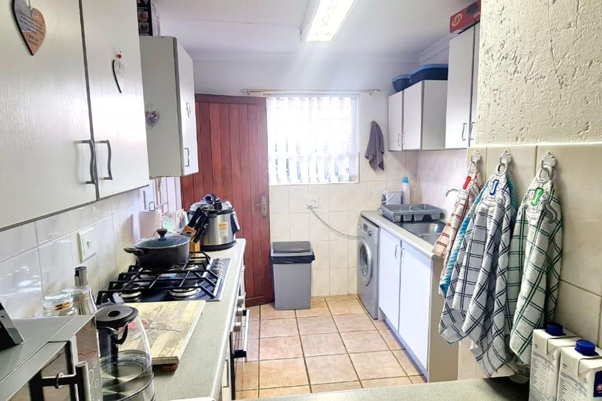 Functional kitchen featuring built-in cabinetry, gas hob, tiled backsplash, and dedicated laundry plumbing connections with direct access to the exterior.