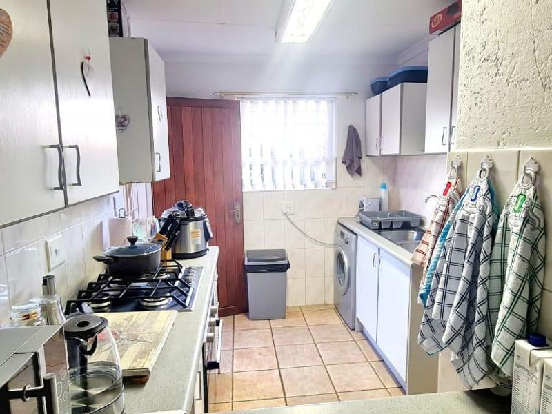 Functional kitchen featuring built-in cabinetry, gas hob, tiled backsplash, and dedicated laundry plumbing connections with direct access to the exterior.