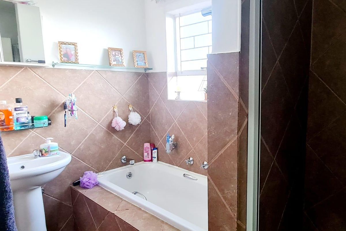 A functional bathroom featuring a built-in bathtub with tiled surround, a pedestal basin, and a window with security bars.