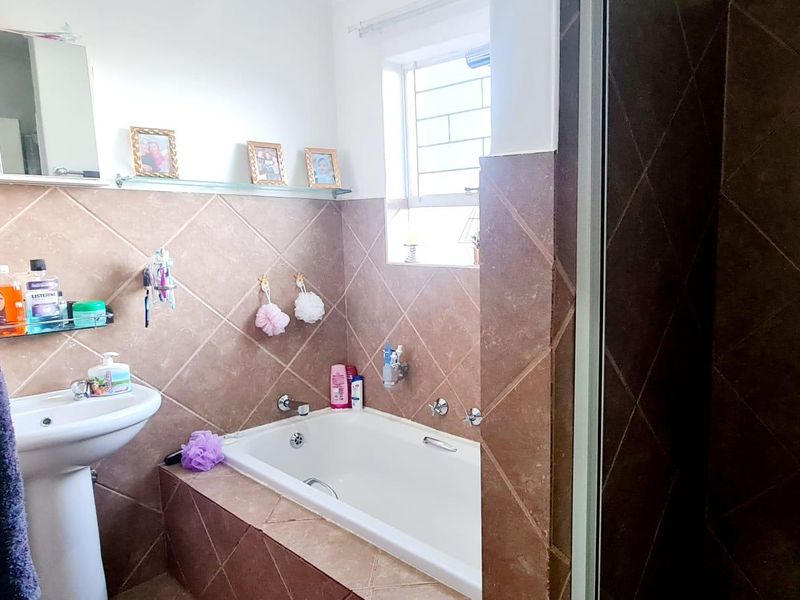 A functional bathroom featuring a built-in bathtub with tiled surround, a pedestal basin, and a window with security bars.