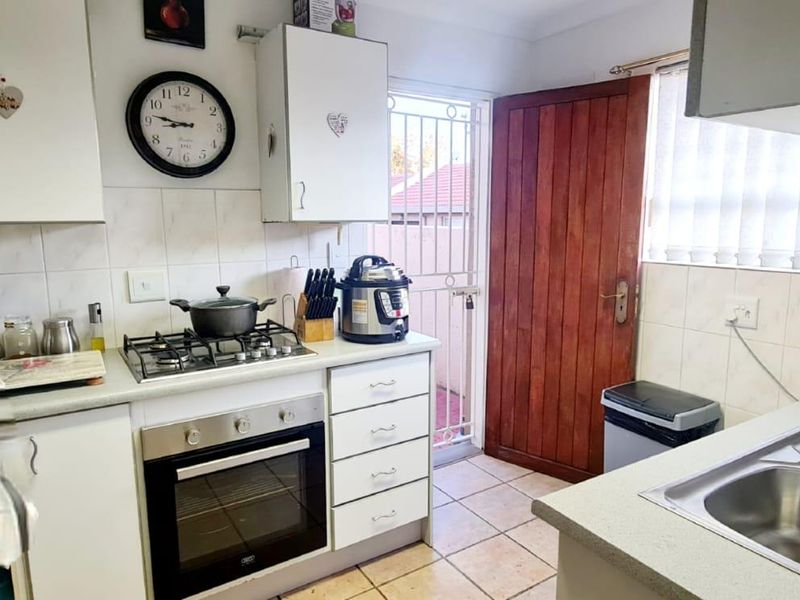 Functional kitchen featuring white cabinetry, gas hob, built-in oven, double stainless steel sink, and direct access to the exterior via a security gate.