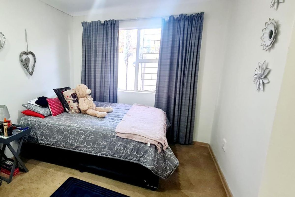 A standard bedroom featuring carpeted flooring and a window fitted with security bars.