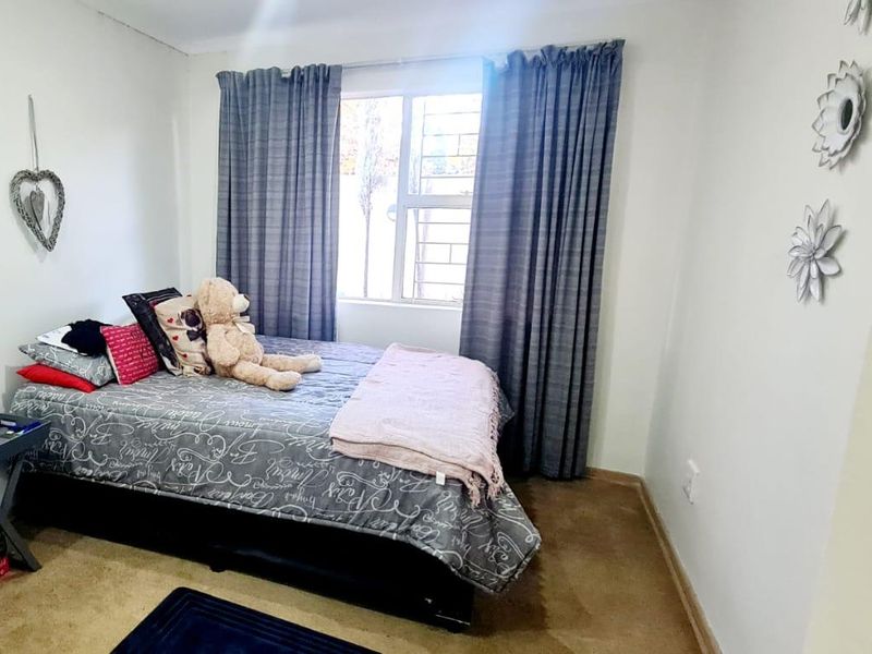 A standard bedroom featuring carpeted flooring and a window fitted with security bars.