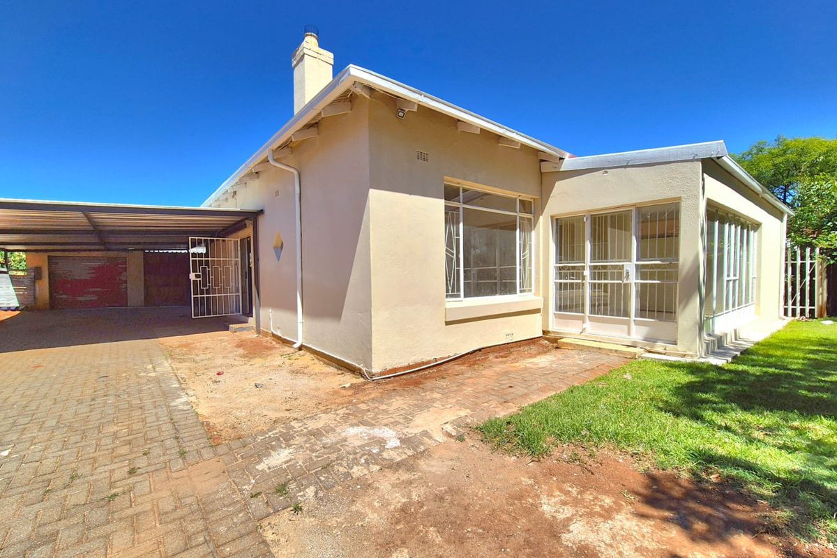 Rear view of the property featuring a carport, paved driveway area, and an enclosed patio with security gates.