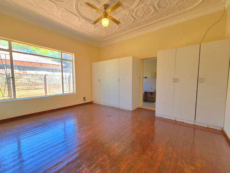Spacious bedroom featuring polished hardwood floors, ornate ceiling detailing, built-in cupboards, and a large window providing natural light.