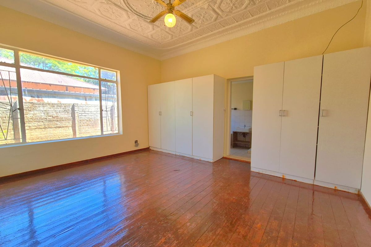 Spacious bedroom featuring polished hardwood floors, ornate ceiling detailing, built-in cupboards, and a large window providing natural light.