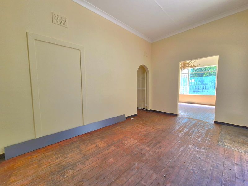An empty living room featuring original timber flooring, coved cornicing, and an arched doorway leading to an adjacent sunroom area.