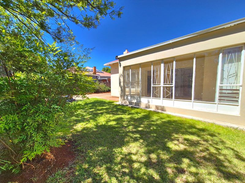 Rear view of the property featuring a lawned garden and an enclosed patio area with security gates and sliding glass doors.
