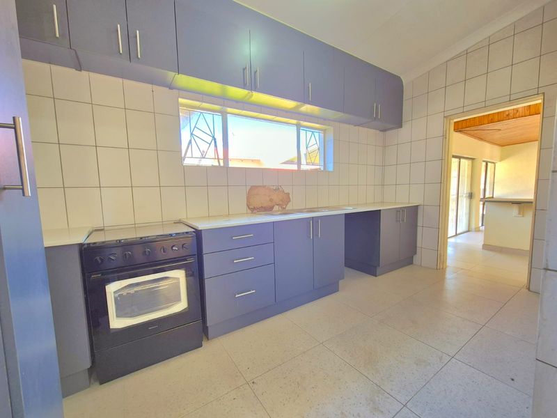 A functional kitchen featuring blue built-in cabinetry, a freestanding oven, tiled splashbacks, and neutral floor tiles, offering a clean canvas for updates.