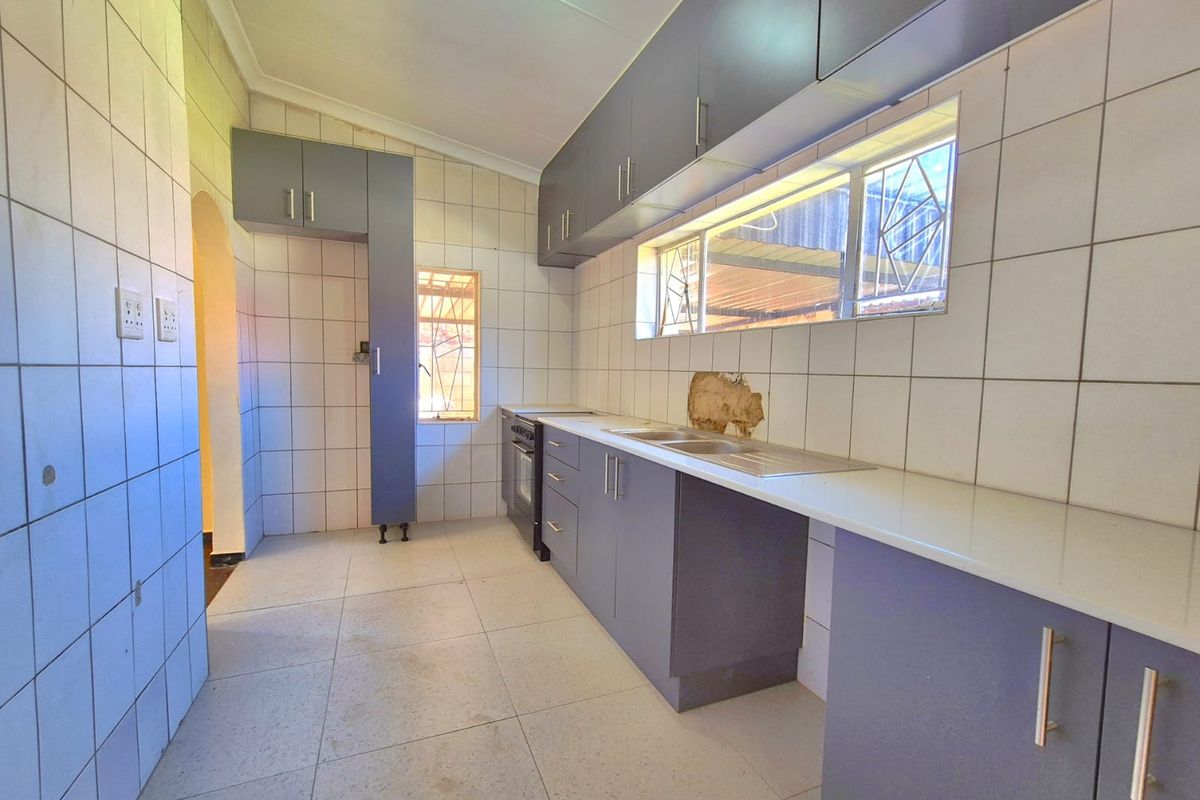 A functional kitchen featuring grey built-in cabinetry, a stainless steel sink, and tiled finishes, currently vacant and ready for updates.