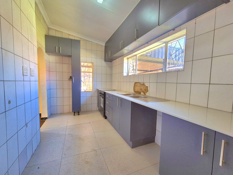A functional kitchen featuring grey built-in cabinetry, a stainless steel sink, and tiled finishes, currently vacant and ready for updates.