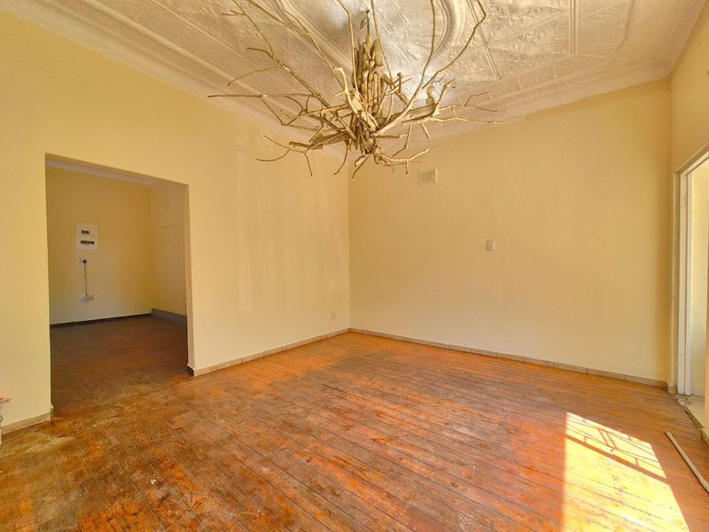 An empty living room featuring original pressed metal ceilings and worn timber flooring, offering a blank canvas for renovation.
