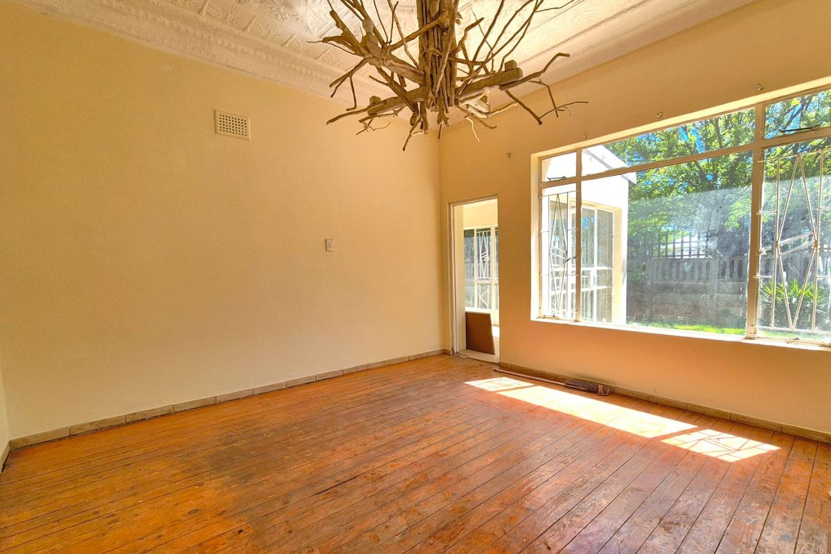 A spacious, empty living room featuring original pressed metal ceilings, large windows providing natural light, and worn timber flooring ready for restoration.