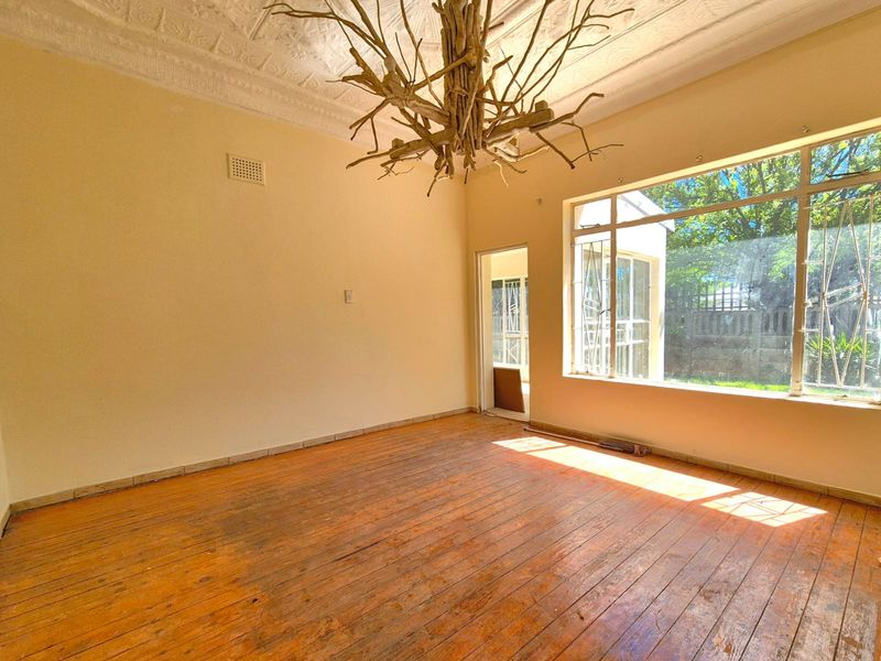 A spacious, empty living room featuring original pressed metal ceilings, large windows providing natural light, and worn timber flooring ready for restoration.