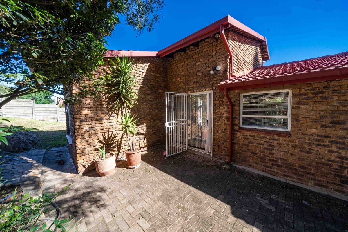 A well-maintained rear exterior view featuring a face brick facade, tiled roof, and a paved patio area with secure access.