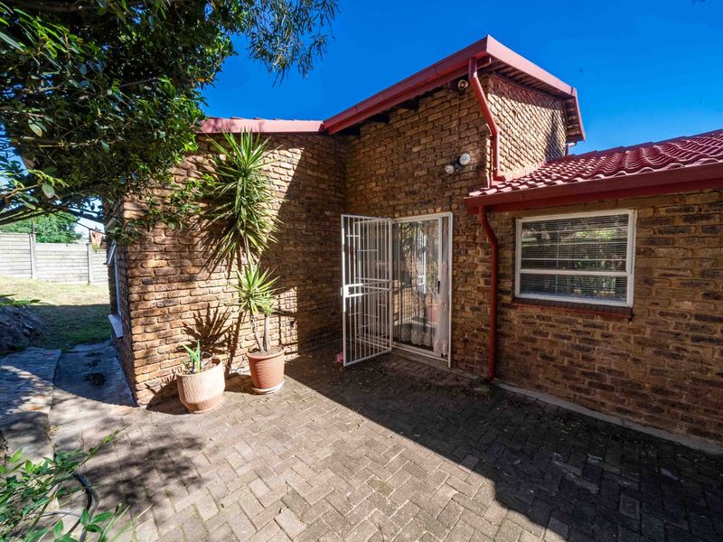 A well-maintained rear exterior view featuring a face brick facade, tiled roof, and a paved patio area with secure access.