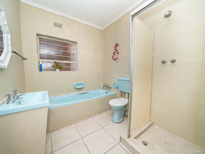 A dated bathroom featuring a blue bathtub and toilet, a separate shower enclosure, and tiled finishes, offering significant potential for a modern renovation.