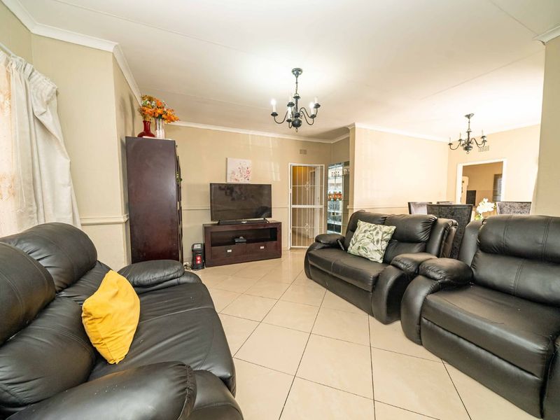 Spacious living room featuring tiled flooring, decorative cove cornicing, and a classic chandelier, providing a comfortable and functional central gathering area.