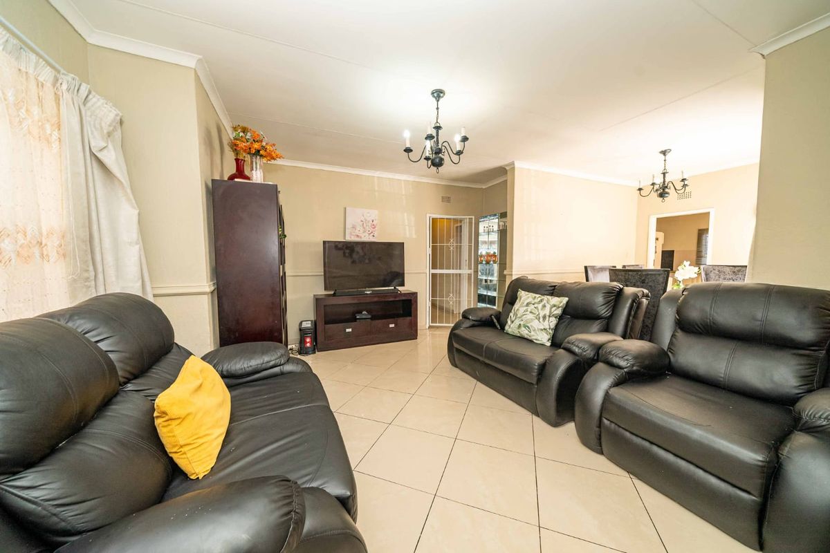 Spacious living room featuring tiled flooring, decorative cove cornicing, and a classic chandelier, providing a comfortable and functional central gathering area.