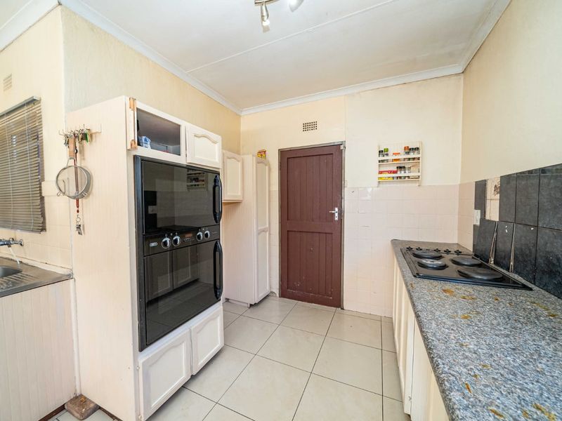 A functional kitchen featuring built-in oven, hob, double sink, and tiled finishes, offering potential for modernization and aesthetic updates.