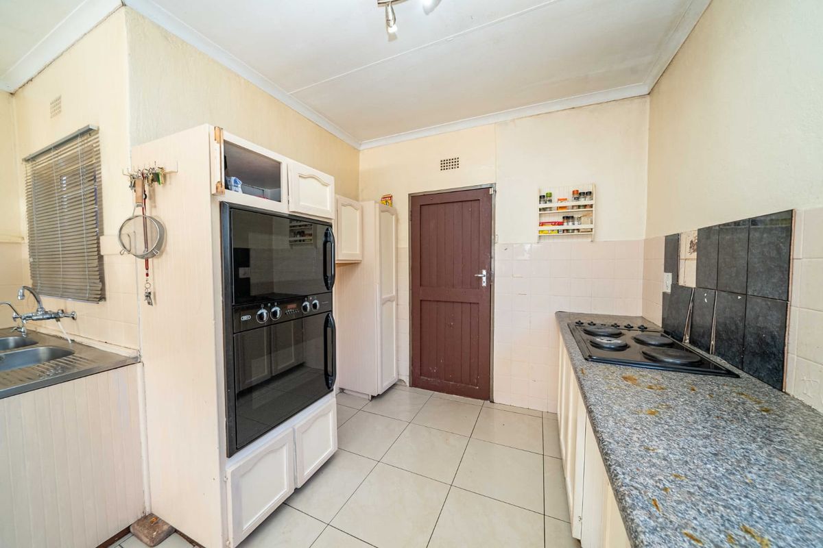A functional kitchen featuring built-in oven, hob, double sink, and tiled finishes, offering potential for modernization and aesthetic updates.