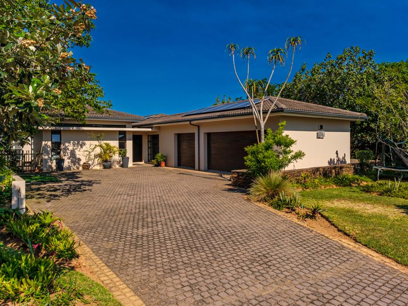 A well-maintained single-story home featuring a paved driveway, double garage, and solar panels, set within a landscaped garden.