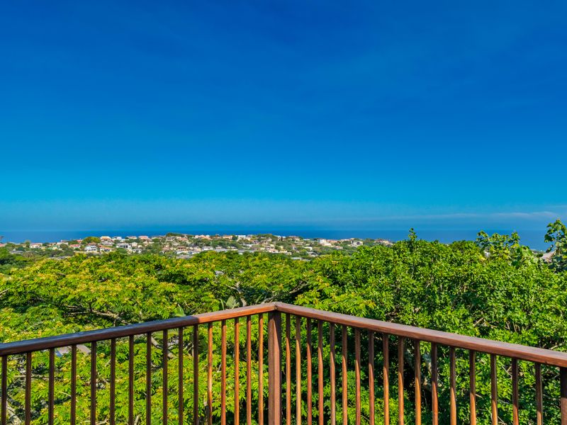 Elevated outdoor view featuring a wooden balustrade overlooking lush greenery and a distant coastal residential landscape.
